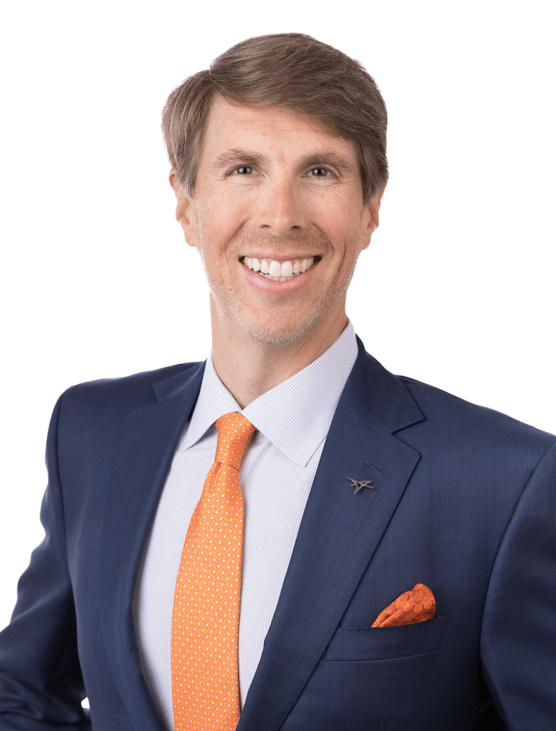 Smiling man in a navy suit with an orange tie and matching pocket square against a white background