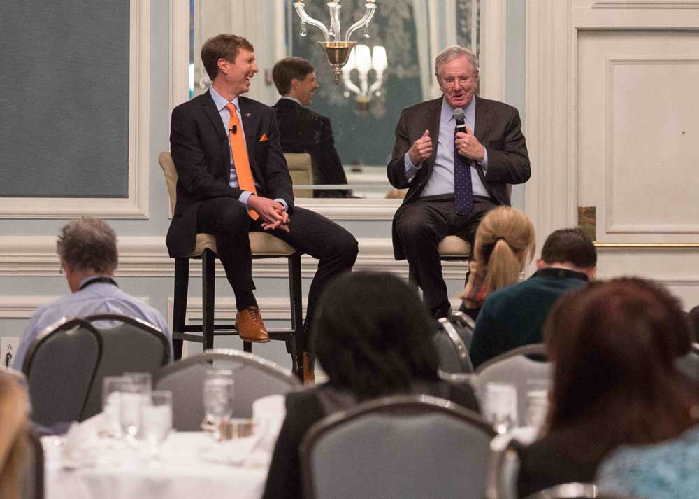 Adam speaking on stage with Steve Forbes